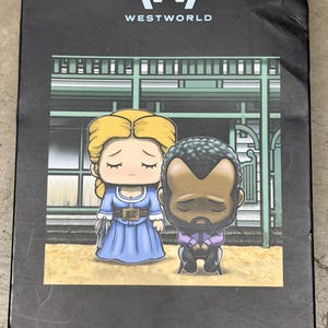 Op de afbeelding: Zwarte doos met het "W" Westworld-logo. Daaronder een cartoon illustratie van Dolores in een blauwe jurk en Arnold in een paars pak. De tekst "Dolores & Arnold" staat onderaan.