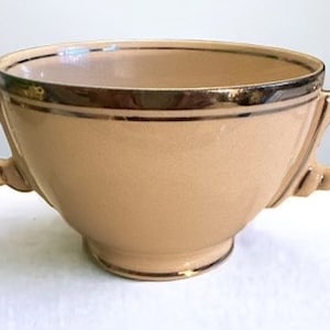 May include: A pale yellow ceramic bowl with two handles and a gold trim around the rim. The bowl is a vintage style.