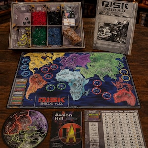 May include: Risk 2210 A.D. board game set including a world map game board, a compartmentalized storage box with colored plastic units, a rulebook, a circular moon map, an Avalon Hill manual, and a numbered army status report tracking sheet.