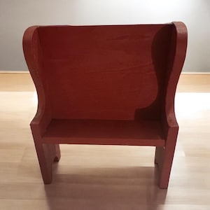 May include: A small, red wooden bench with a high back and a shelf underneath. The bench is made of solid wood and has a simple, rustic design.