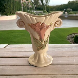 May include: A cream-coloured ceramic vase with a pink and green floral design. The vase has two handles and a flared top.
