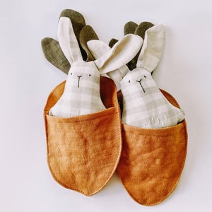May include: Two plush bunny toys with gingham fabric and embroidered faces, nestled in brown fabric pouches.