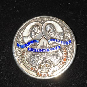 以下が含まれることがあります： 「DAILY DISPATCH BIRTHDAY CLUB」と「FOUNDED IN 1913」の文字が入った、丸い銀色のピンバッジ。2つの肖像画と王冠が特徴です。テキストは青と赤のエナメルです。