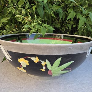 Op de afbeelding: Een grote keramische kom met een zwarte buitenkant, handbeschilderd met gele bloemen en groene bladeren. De rand is lichtgrijs en de binnenkant heeft een levendige limoengroene basis met zwarte en rode geometrische randaccenten.