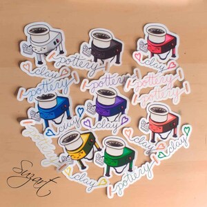 May include: Nine colorful stickers featuring a cartoon illustration of a pottery wheel with the text "I love pottery" and "I love clay" written in cursive.