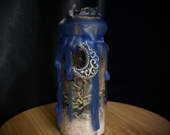 May include: A small glass bottle filled with herbs and sand, sealed with blue wax and a silver crescent moon charm.