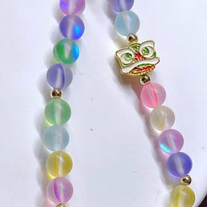 May include: A vibrant beaded bracelet with iridescent, spherical beads in yellow, pink, green, blue, and purple. The bracelet has gold-coloured accents and a gold-toned charm with a lion design.