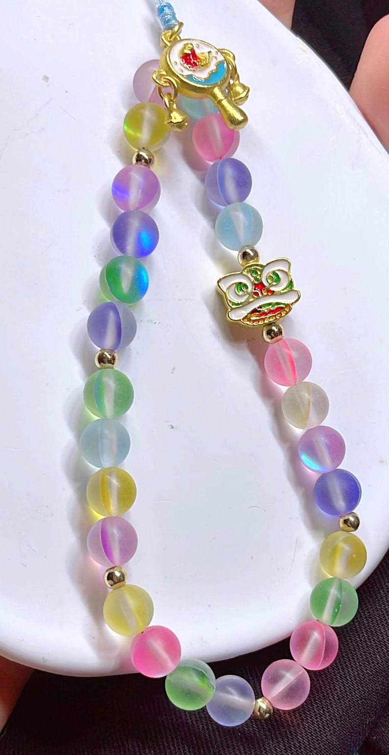May include: A vibrant beaded bracelet with iridescent, spherical beads in yellow, pink, green, blue, and purple. The bracelet has gold-coloured accents and a gold-toned charm with a lion design.