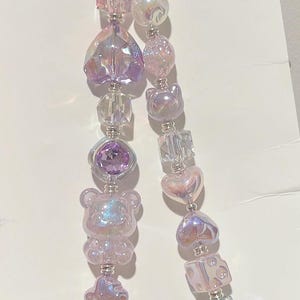 May include: A purple and iridescent charm bracelet with a variety of beads, including hearts, bears, and dice. The bracelet is attached to a purple ring.