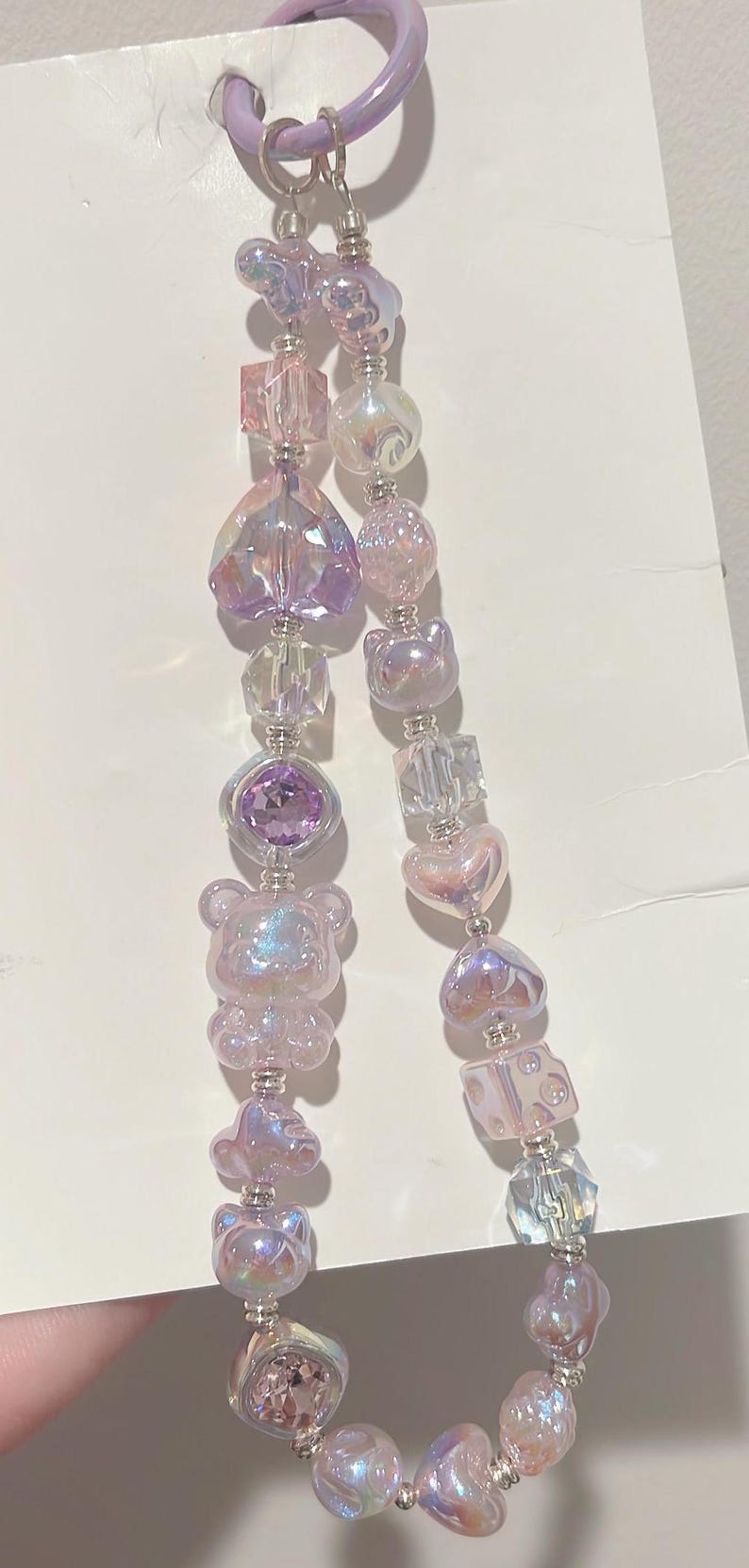 May include: A purple and iridescent charm bracelet with a variety of beads, including hearts, bears, and dice. The bracelet is attached to a purple ring.
