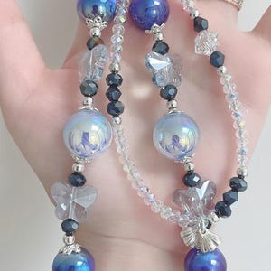 May include: A beaded keychain featuring iridescent blue and silver beads, clear faceted beads, and butterfly charms. The keychain has a silver clasp and is designed with multiple strands of beads.