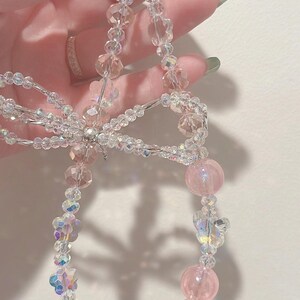 May include: A pink and clear crystal beaded keychain with a silver clasp and a bow in the center.