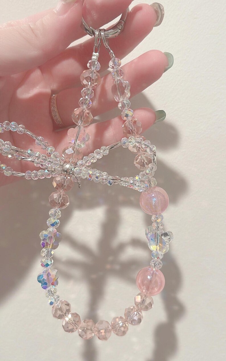 May include: A pink and clear crystal beaded keychain with a silver clasp and a bow in the center.