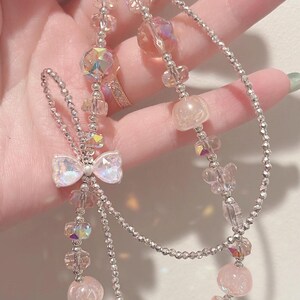 May include: A silver charm bracelet with pink and iridescent crystal beads, a pink bow charm, and a clear bear charm.