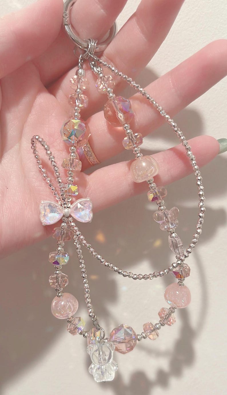 May include: A silver charm bracelet with pink and iridescent crystal beads, a pink bow charm, and a clear bear charm.