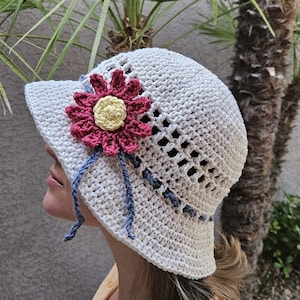 May include: A white crocheted sun hat with a pink and yellow flower embellishment. The hat has a wide brim and a crocheted design.