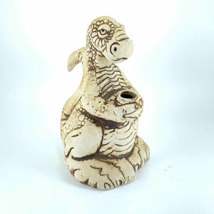 May include: A ceramic dragon sculpture with a textured surface and brown accents. The dragon is curled up with its tail wrapped around its body. The dragon has a small hole in its back, which could be used for incense or a small plant.