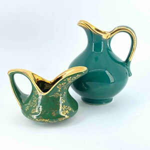 Puede incluir: Dos jarras de crema de cer&aacute;mica verde con detalles dorados y dise&ntilde;os florales. La jarra m&aacute;s peque&ntilde;a tiene un dise&ntilde;o m&aacute;s moderno con un asa curva. La jarra m&aacute;s grande tiene un dise&ntilde;o m&aacute;s tradicional con un asa recta.