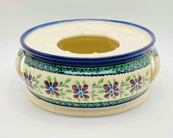 Könnte beinhalten: Ein weißer Keramiktopf mit blauen und grünen Blumendesigns und zwei Griffen. Der Topf hat einen erhöhten Mittelteil mit einem Loch in der Mitte.