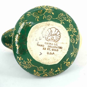 Puede incluir: Tetera de cer&aacute;mica verde y dorada con un dise&ntilde;o floral. La parte inferior de la tetera tiene el texto "Pearl China Co. Hand Decorated 22 Kt. Gold U.S.A."
