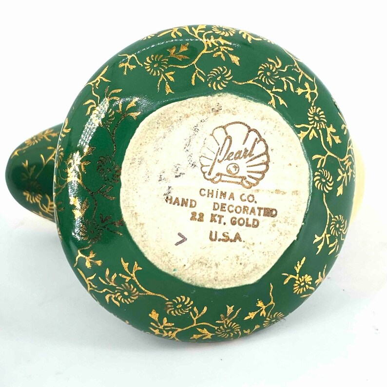 Puede incluir: Tetera de cer&aacute;mica verde y dorada con un dise&ntilde;o floral. La parte inferior de la tetera tiene el texto "Pearl China Co. Hand Decorated 22 Kt. Gold U.S.A."