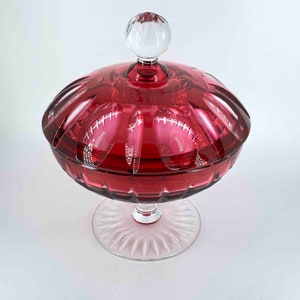 Puede incluir: Un plat de dulces de vidrio vintage con una tapa transparente y una base roja. El plato tiene una base de pedestal y un dise&ntilde;o decorativo de vidrio cortado.