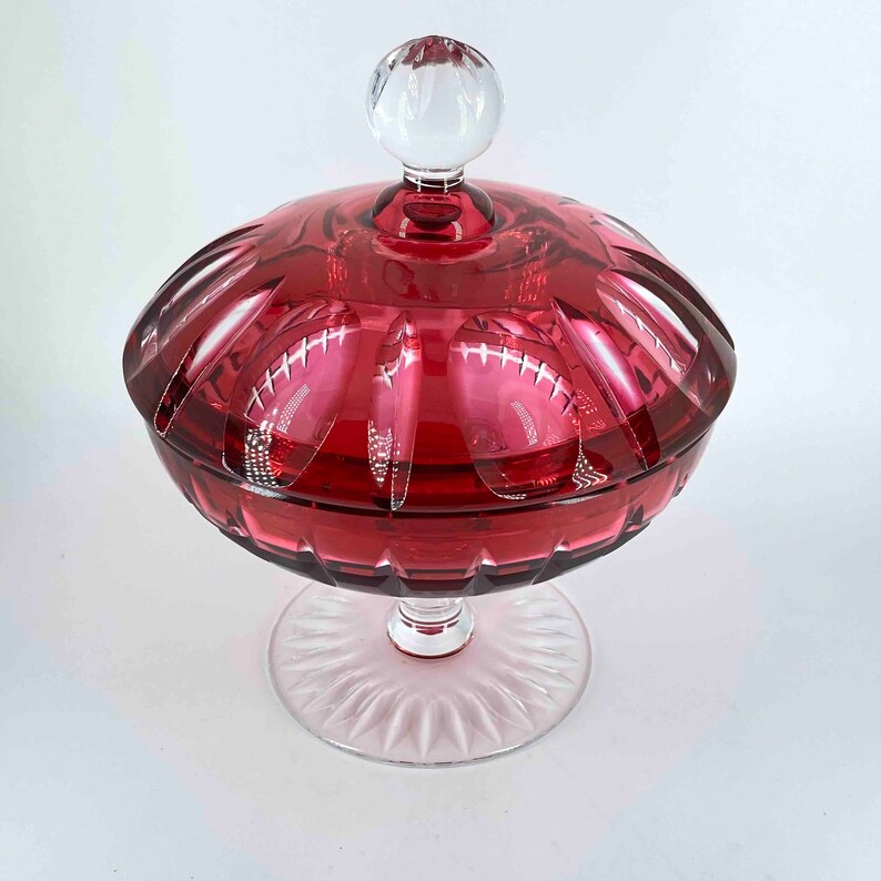 Puede incluir: Un plat de dulces de vidrio vintage con una tapa transparente y una base roja. El plato tiene una base de pedestal y un dise&ntilde;o decorativo de vidrio cortado.