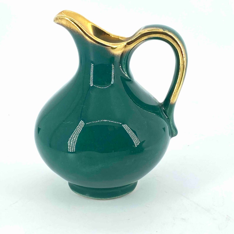Puede incluir: Una peque&ntilde;a jarra de cer&aacute;mica verde con un borde y un asa dorados. La jarra tiene un cuerpo redondo y un peque&ntilde;o pico.