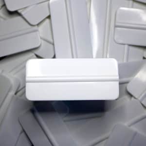 May include: A close-up of a white plastic squeegee with a single blade. The squeegee is surrounded by other white squeegees.