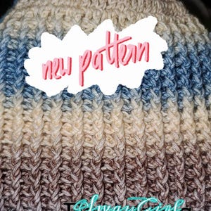 May include: A close-up of a crocheted hat with a blue, brown, and beige color gradient. The hat has a textured stitch pattern and the text "new pattern" is written on a white sticker.