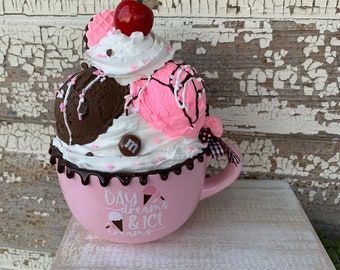May include: A pink ceramic mug with a chocolate drizzle and a white and pink ice cream cone design. The mug has the text "Day dreams & ice cream" on it.