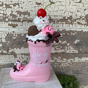 May include: Pink boot shaped ceramic planter with a white and pink ice cream cone design. The planter has the text "Life is better with ice cream" on the side.