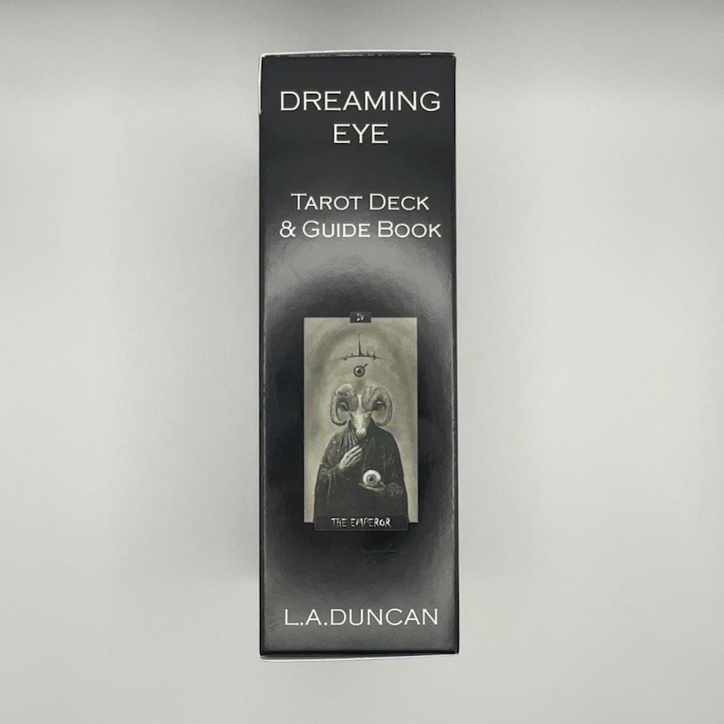 May include: A black tarot deck box with the words "Dreaming Eye" and "Tarot Deck & Guide Book" in white. The box features an illustration of a figure with ram horns and the text "The Emperor". The author's name, L.A. Duncan, is printed at the bottom.