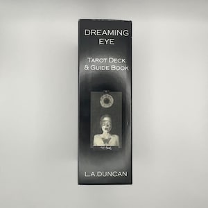 May include: A black tarot card box with the words "DREAMING EYE" and "TAROT DECK & GUIDE BOOK" in white. The box features an illustration of a person with a butterfly on their chest. The text "THE fool" is below the illustration. The author's name, "L.A.DUNCAN", is at the bottom.