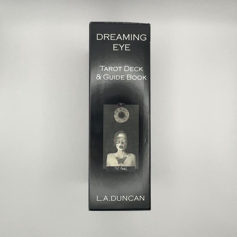 May include: A black tarot card box with the words "DREAMING EYE" and "TAROT DECK & GUIDE BOOK" in white. The box features an illustration of a person with a butterfly on their chest. The text "THE fool" is below the illustration. The author's name, "L.A.DUNCAN", is at the bottom.