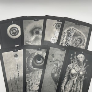 May include: A collection of tarot cards with dark, grayscale illustrations. Each card features a unique, detailed drawing, including eyes, tentacles, and figures, with titles like "Swords" and numbers at the top.