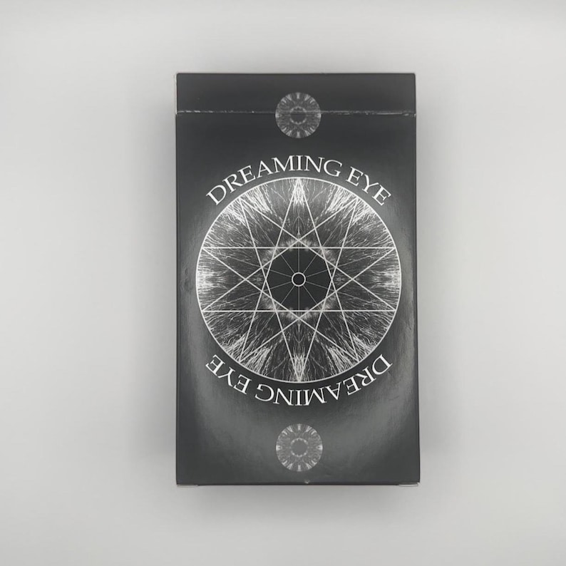 May include: A black rectangular box with the words "Dreaming Eye" in white lettering. A silver geometric design is centered on the front. Two silver circular designs are at the top and bottom of the box.