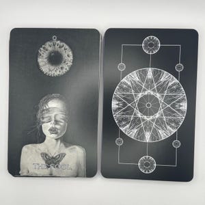 Può includere: Due carte dei tarocchi con sfondi neri. Una carta presenta un'illustrazione in scala di grigi di una persona con una farfalla e la scritta "THE FOOL". L'altra carta ha un design geometrico con un cerchio centrale e linee radiali.