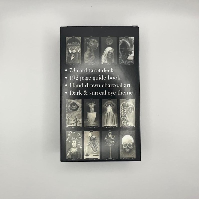 May include: A black tarot card box with a dark and surreal eye theme. The box features hand-drawn charcoal art and includes a 78-card tarot deck and a 192-page guide book. The box has a series of black and white images.