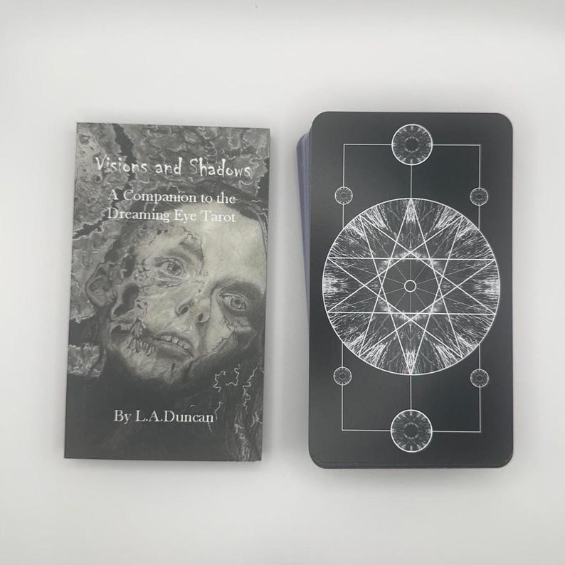 May include: A tarot deck and companion book set. The book cover features a grayscale portrait with the text "Visions and Shadows" and "A Companion to the Dreaming Eye Tarot". The deck has black cards with a white geometric design.
