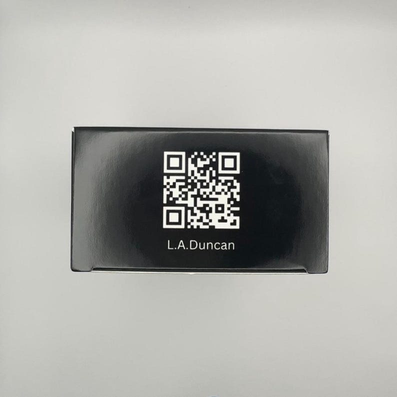 May include: A black box with a QR code and the text "L.A.Duncan" printed in white. The box is rectangular and appears to be made of cardboard or a similar material. The background is a light gray color.