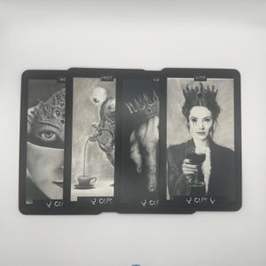 May include: A set of four tarot cards with black borders. Each card features a detailed grayscale illustration. The cards are labeled "PAQ", "NIGHT", "ASH", and "QUEEN", with the suit "Cups" at the bottom. The artwork has a gothic, fantasy theme.