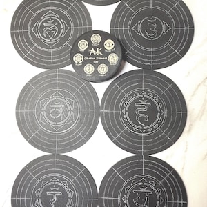 以下が含まれることがあります： 白線デザインのダークグレーのチャクラステンシルコレクション。 ステンシルは円形で、さまざまなチャクラのシンボルと「AK Chakra Stencil Set」のテキストが特徴です。 ステンシルは明るい色の表面に配置されています。