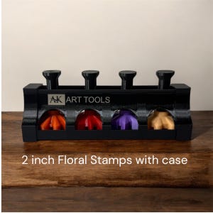 May include: A black case containing four floral stamps, each approximately 5 cm in diameter, in orange, red, purple, and tan. The case is labelled "AK ART TOOLS". Ideal for crafting and art projects.