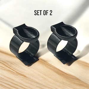 May include: Set of two black plastic ring holders. Each holder has a small, round, indented area on top.