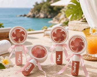 May include: Four portable handheld fans with circular heads and terracotta-colored blades. Each handle features a unique name in white script: Claire, Olivia, Mia, and Audrey. The fans are decorated with light pink ribbons tied around the handles.