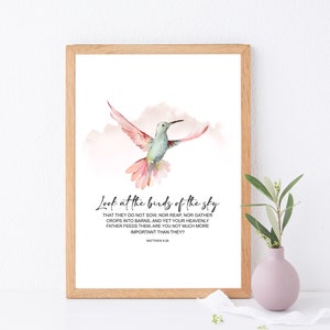 Puede incluir: Una pintura de acuarela de un colibrí en vuelo contra un cielo nublado rosa y blanco. La pintura incluye una cita de Mateo 6:26: "Mirad las aves del cielo..."