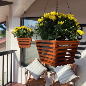 May include: Two hanging wooden planters with yellow flowers. The planters are made of wood slats and have a rectangular shape. The planters are hanging from chains.