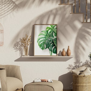 May include: A framed print of a green monstera leaf against a white background, displayed on a shelf with two ceramic vases and a bouquet of dried wheat.