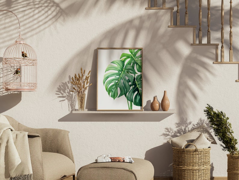 May include: A framed print of a green monstera leaf against a white background, displayed on a shelf with two ceramic vases and a bouquet of dried wheat.